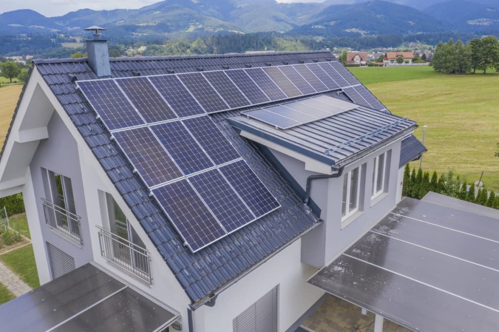 Modern house with multiple solar panels installed on the roof, surrounded by green fields and mountains in the background. Increasingly, British homeowners are getting solar panels to embrace sustainable living and reduce energy costs.