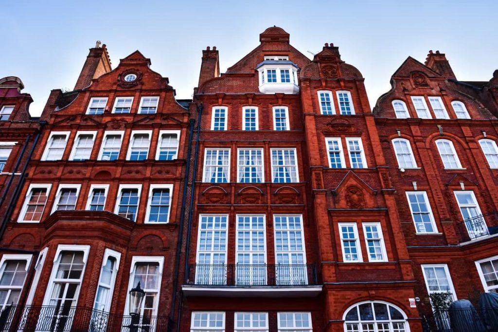 Red brick flat buildings with large white-trimmed windows and ornate architectural details, photographed from a low angle against a clear blue sky, showcase the importance of historic home preservation.
