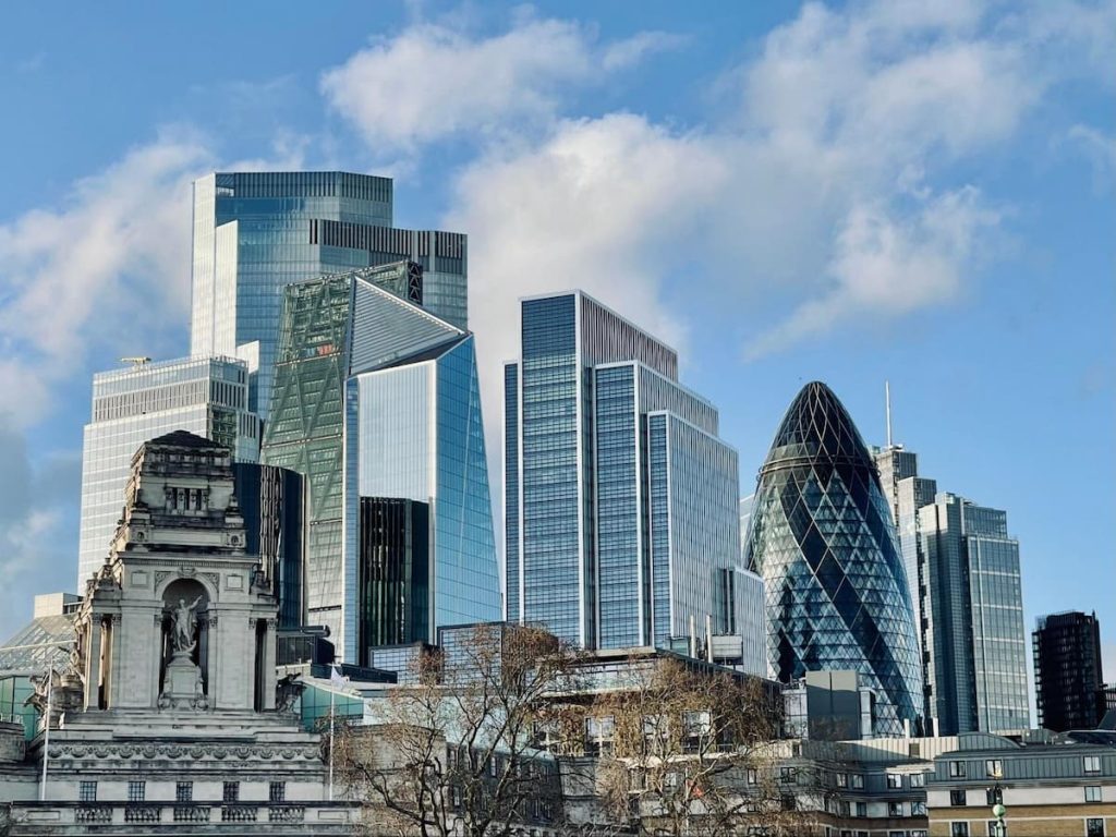 Modern skyscrapers and historic buildings stand together in London’s financial district, featuring glass façades and the distinctive Gherkin building under a partly cloudy sky—a cityscape often brought to life through 3D exterior design rendering for development tenders.