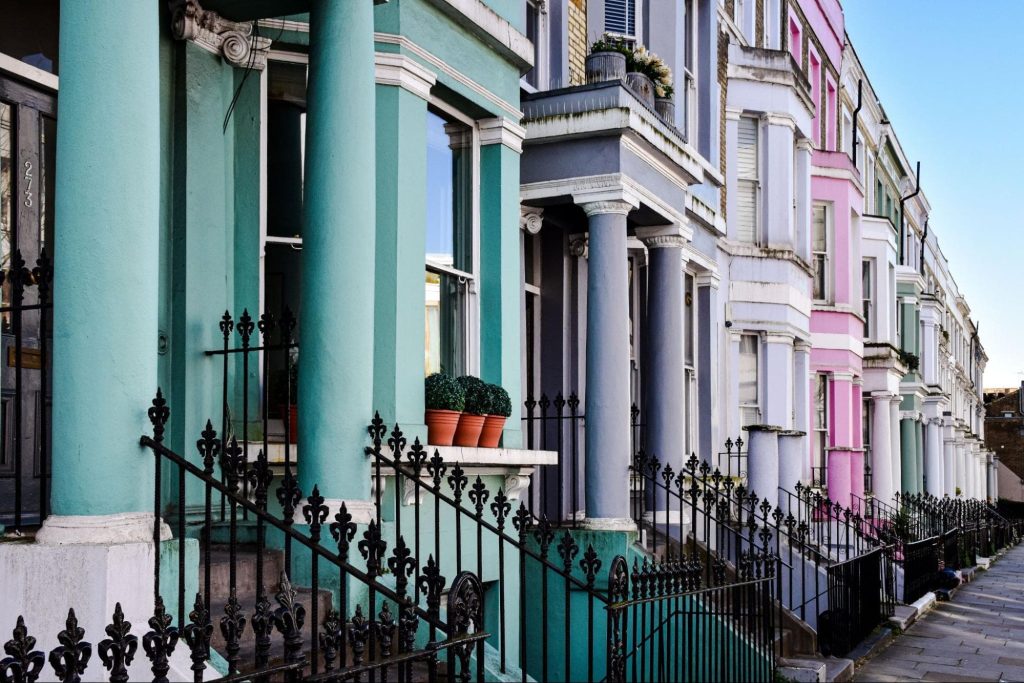 A row of colourful terraced houses with iron railings, columns, bay windows, and potted plants on the steps under a clear sky—an ideal scene for housebuilding visualisation projects in 2026.