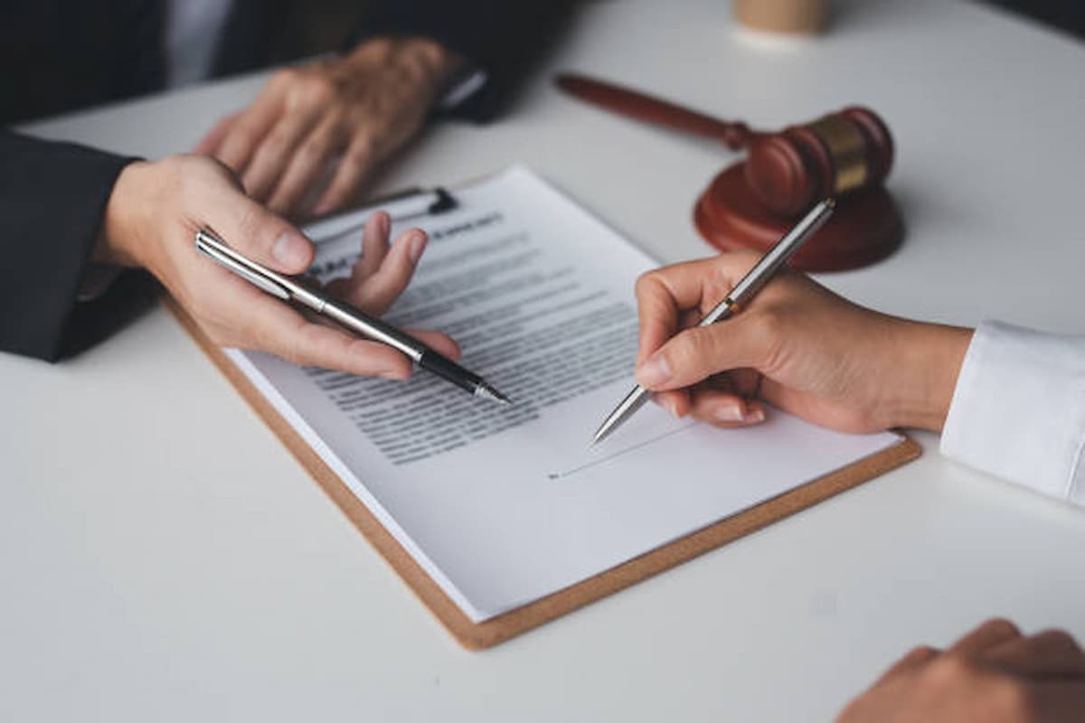 Two people review and sign a document on a clipboard at a desk, with a wooden judge’s gavel nearby—demonstrating how businesses can carefully document procedures to prevent legal actions, often with guidance from Equality Act inspectors.