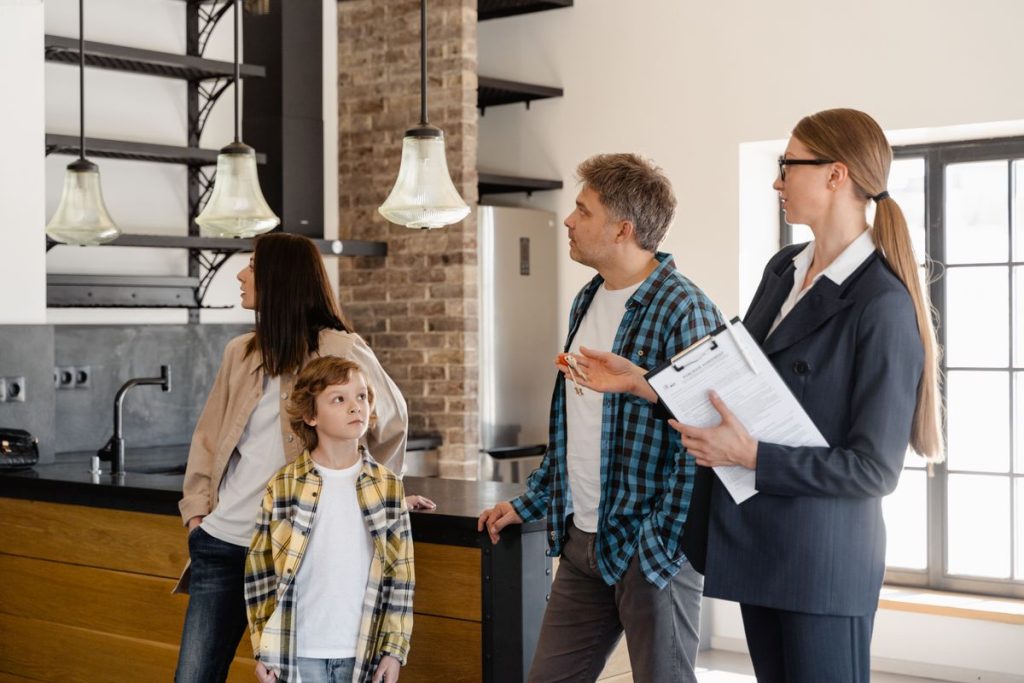 An estate agent shows a modern kitchen to a family of three, including a young boy, during a house viewing, while explaining the buyer's guide and the key steps from offer to completion in UK conveyancing.