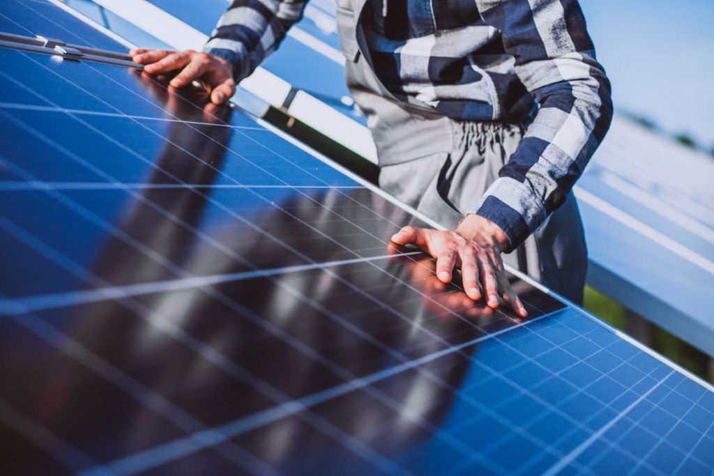Person inspecting or cleaning a solar panel outdoors on a sunny day, with their hands touching the surface and solar panels visible in the background—perfectly capturing the careful attention of experienced solar panel installers London trusts for professional solar panel installation.