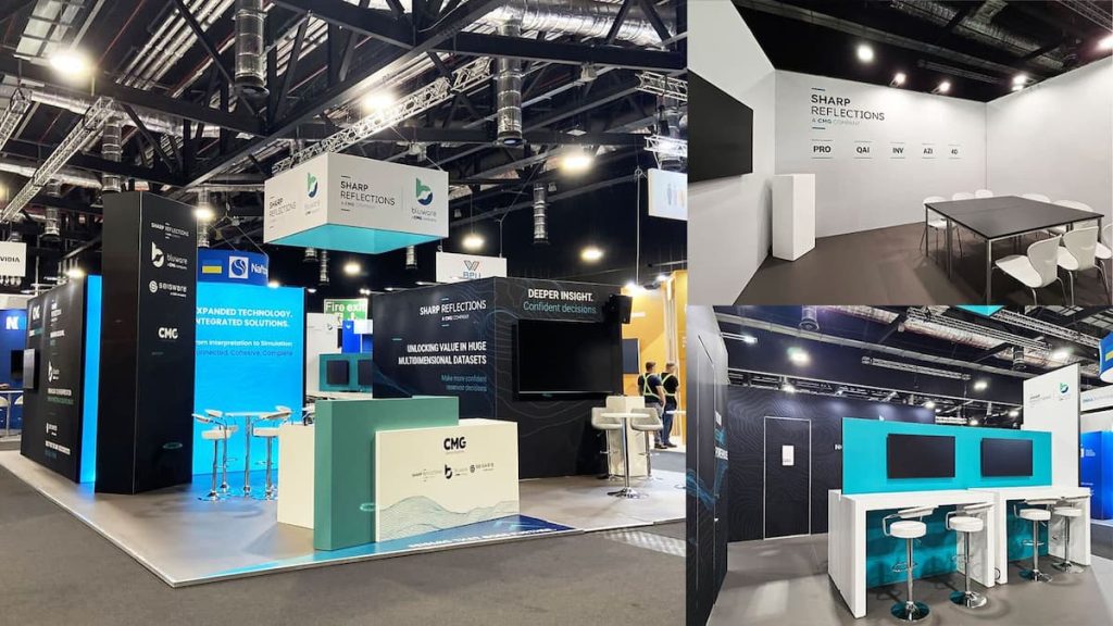A trade show stand with branded panels, seating areas, and computer workstations—crafted using sustainable exhibition stands—features company logos and information under bright overhead lighting.