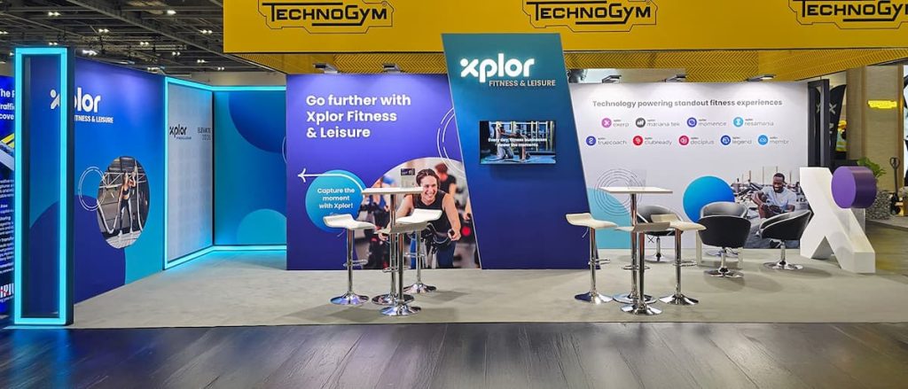 Xplor Fitness & Leisure exhibition stand with seating, digital displays, branded graphics, and informational signage in a convention setting, featuring sustainable exhibition stands designed through expert exhibition stand construction for both style and environmental responsibility.
