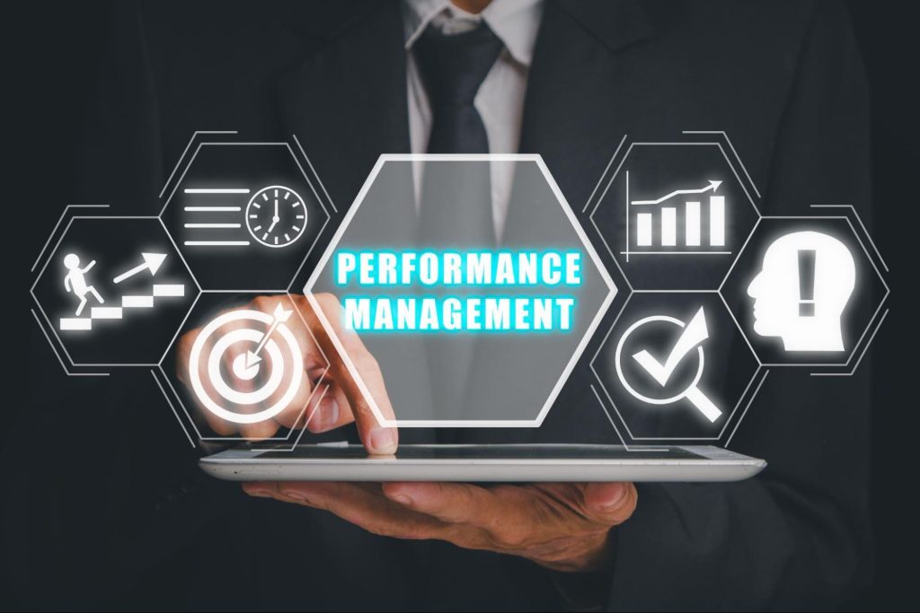 A person in a suit holds a tablet with virtual icons and the words “Performance Management” displayed in the centre, surrounded by business-related graphics that highlight evidenced competence and company compliance.
