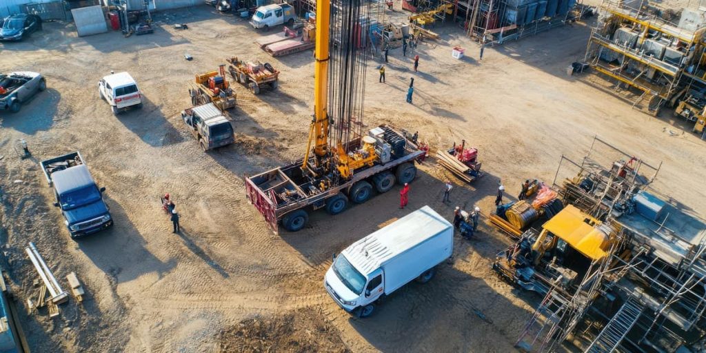 Aerial view of a construction site with workers, vehicles—such as electric vans—machinery, and equipment on an earth surface.