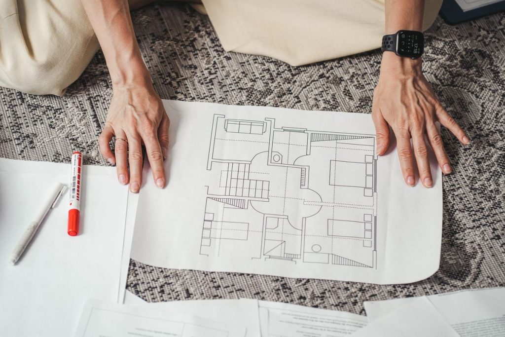 Person holding a printed architectural floor plan on a patterned surface, surrounded by papers, a red marker, and a pen—perfectly capturing the early stages of home design and functional home layout planning.