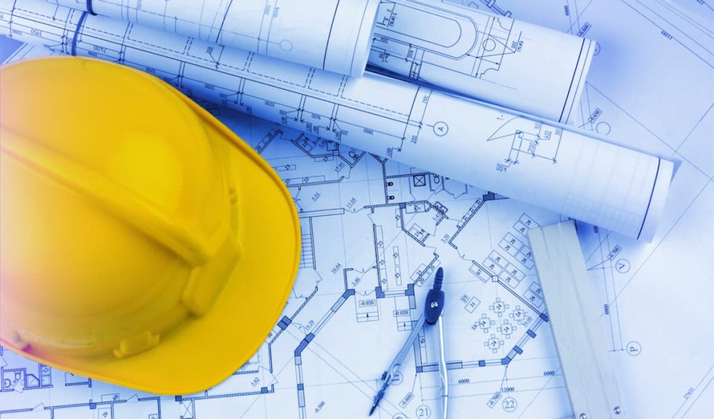 A yellow construction helmet, blueprints, compasses, and ruler are arranged on a table, illustrating how key trends in digital transformation are shaping the future of construction.