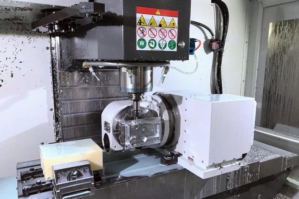 A CNC milling machine operates on a metal workpiece, with safety warning labels visible on the machine and metal swarf scattered around. This advanced setup at WayKen is ideal for producing complex rotational parts through precision mill-turn machining.
