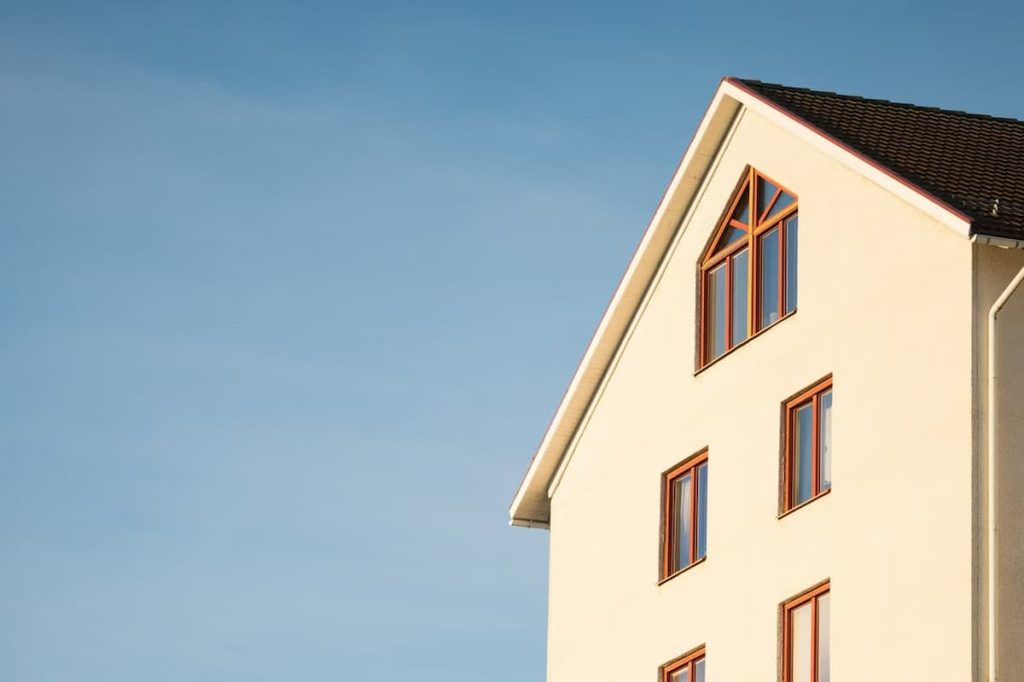 Top portion of a beige multi-storey building with several rectangular and triangular windows, set against a clear blue sky—designed in accordance with Passivhaus principles for exceptional energy efficiency.