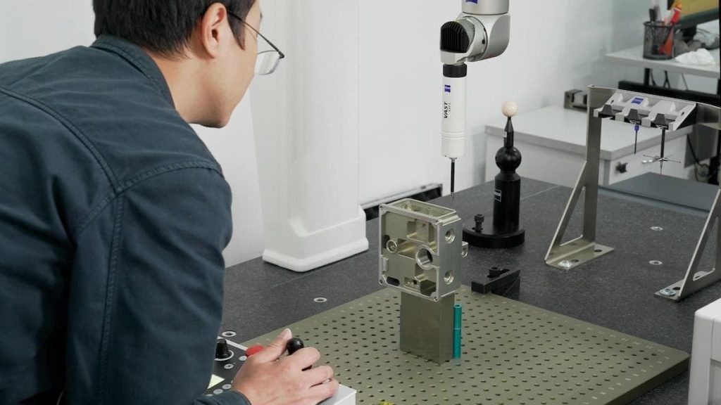 A person operates a coordinate measuring machine analysing a complex rotational part on a perforated work surface in a lab setting, showcasing WayKen’s expertise in mill-turn machining.