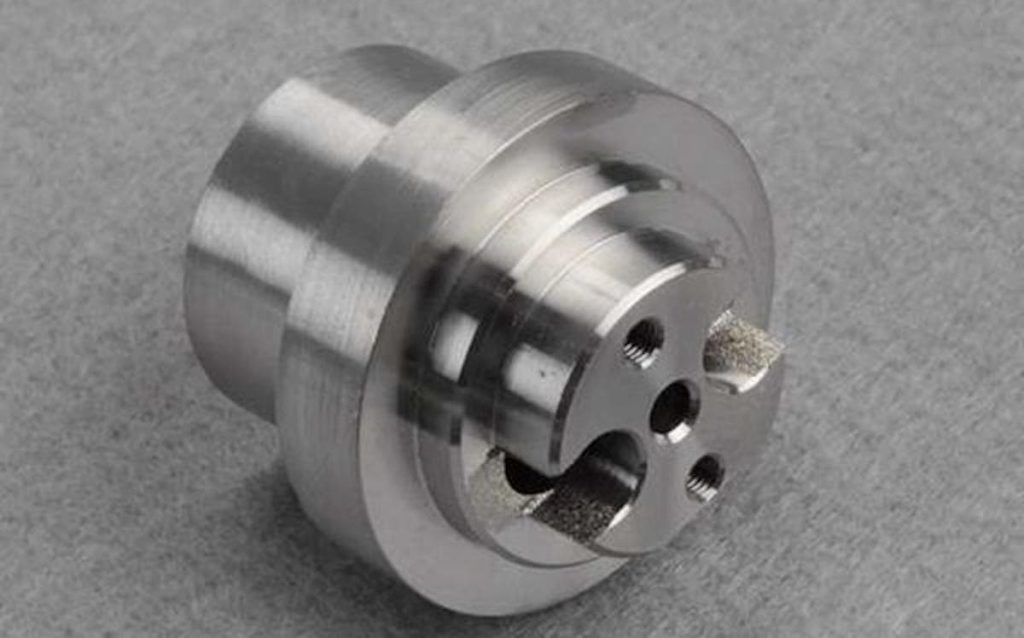 A machined metal component with cylindrical shape, grooves, and multiple holes, expertly crafted using Mill-Turn Machining techniques, rests on a grey surface—showcasing WayKen’s capabilities in producing complex rotational parts.