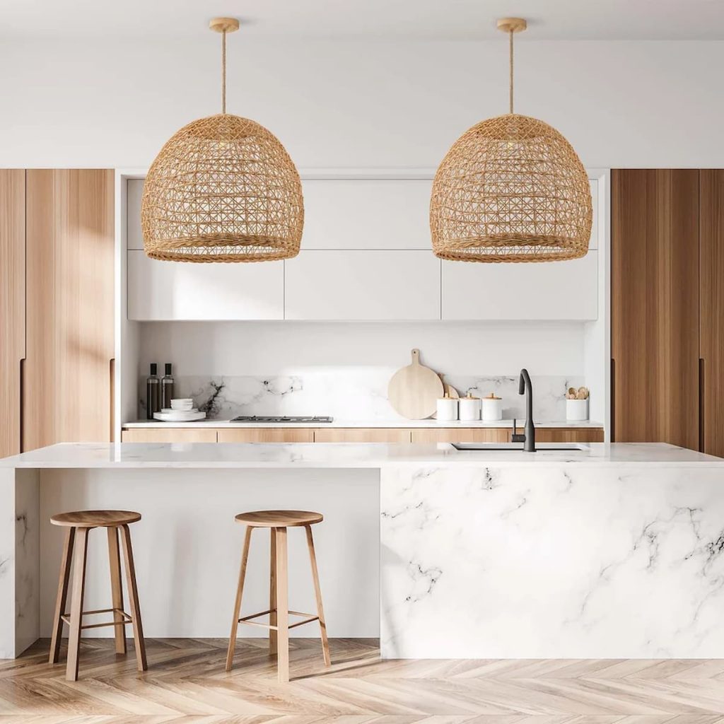 Modern kitchen with marble island, two wooden stools, wood cabinetry, and two woven pendant lights. Neutral tones and minimalist decor create a clean, contemporary look.